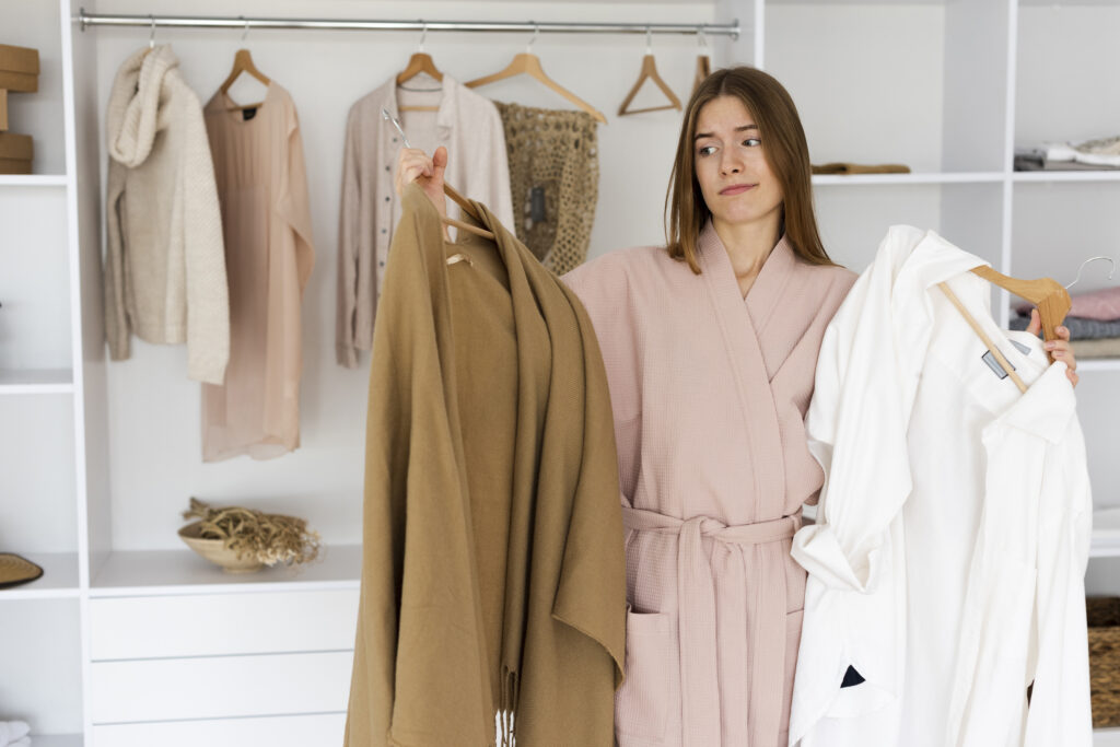 Woman comparing beige and white outfits while deciding on a capsule wardrobe color pallet in a minimalist closet